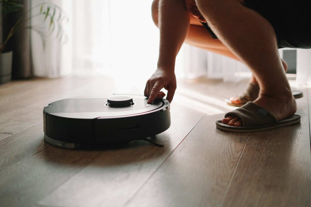 Ruka spouští robotický vysavač na dřevěné podlaze